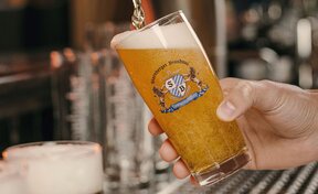 Hand füllt ein Glas mit Bier, auf dem ein Starnberger Brauhaus Logo platziert ist.