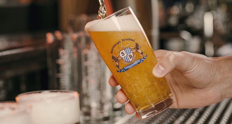 Hand füllt ein Glas mit Bier, auf dem ein Starnberger Brauhaus Logo platziert ist.