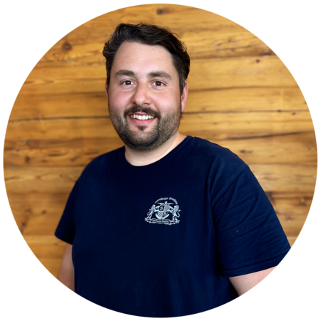 Junger Mann mit dunkelbraunen, leicht gewellten Haaren und einem Dreitagebart, trägt ein dunkelblaues T-Shirt mit dem Starnberger Brauhaus Logo.