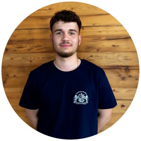 Junger Mann mit dunkelbraunen, lockigen Haaren und einem Bart, trägt ein dunkelblaues T-Shirt mit dem Starnberger Brauhaus Logo.