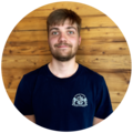 Junger Mann mit dunkelblonden, kurzen Haaren und einem Bart, trägt ein dunkelblaues T-Shirt mit dem Starnberger Brauhaus Logo.