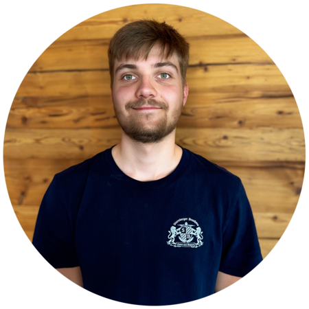 Junger Mann mit dunkelblonden, kurzen Haaren und einem Bart, trägt ein dunkelblaues T-Shirt mit dem Starnberger Brauhaus Logo.