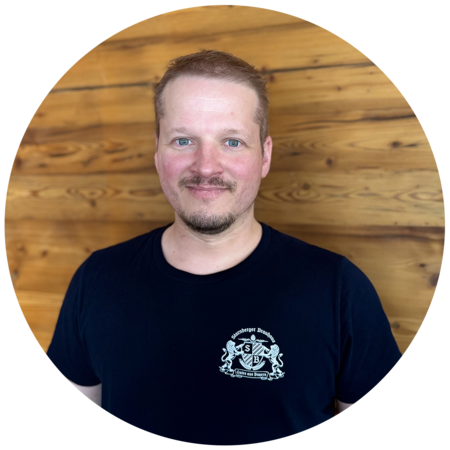 Junger Mann mit mittelblonden Haaren und Bart, trägt ein dunkelblaues T-Shirt mit dem Starnberger Brauhaus Logo.