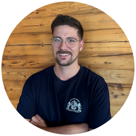 Junger Mann mit dunkelbraunen Haaren, Bart und Brille, trägt ein dunkelblaues T-Shirt mit dem Starnberger Brauhaus Logo.