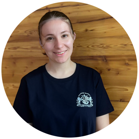 Junge Frau mit zusammengebundenem Haar trägt ein dunkelblaues T-Shirt mit dem Starnberger Brauhaus Logo.