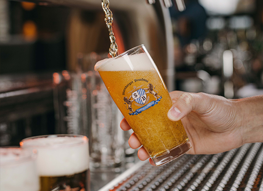 Hand füllt ein Glas mit Bier, auf dem ein Starnberger Brauhaus Logo platziert ist.