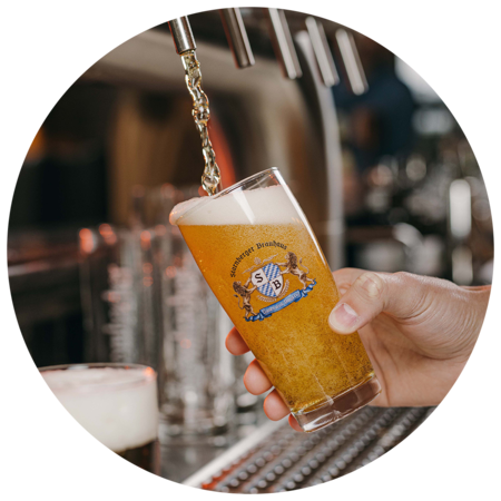 Hand füllt ein Glas mit Bier, auf dem ein Starnberger Brauhaus Logo platziert ist.